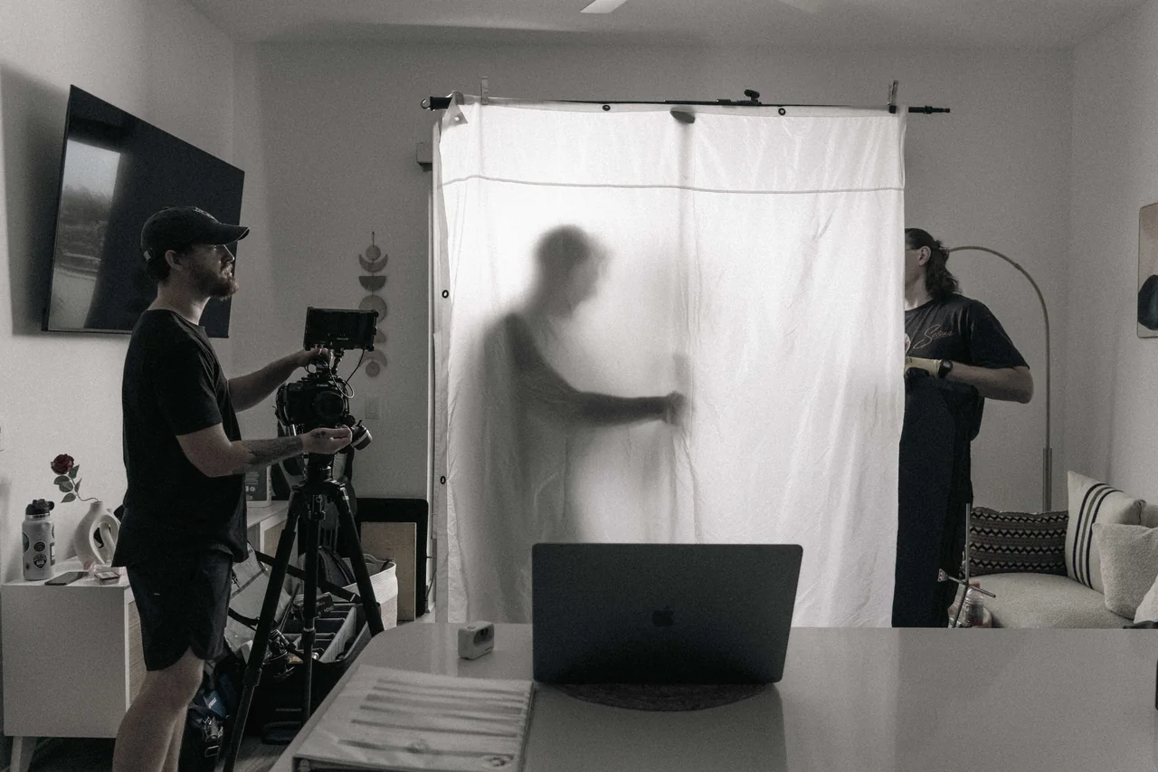 Recovery crew setting up a large diffusion frame beside a cinema camera in an apartment.
